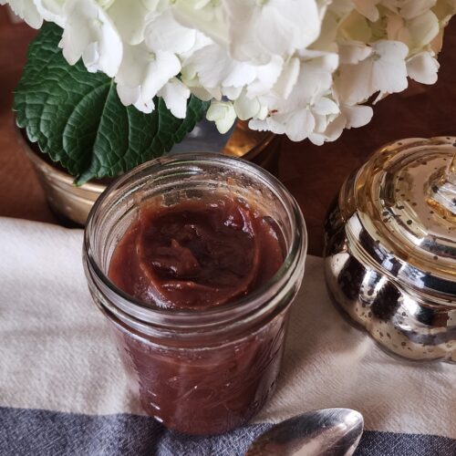 apple butter in a jar on counter with flowers in the background