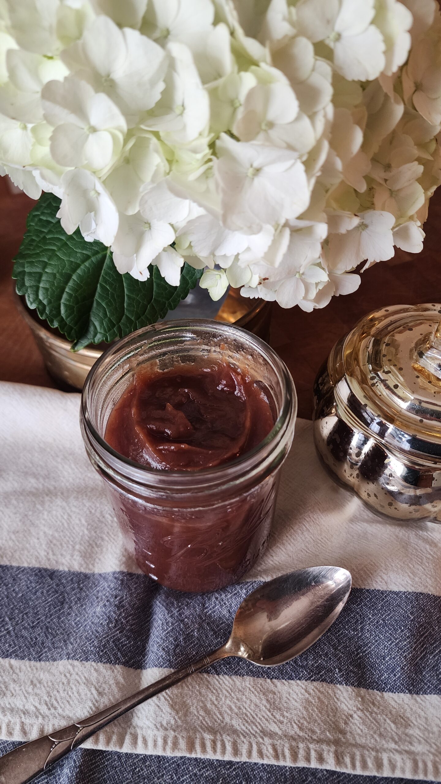 apple butter in a jar on counter with flowers in the background