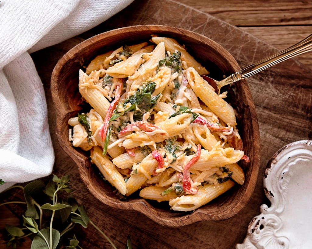 A mouth-watering creamy pasta salad with fresh vegetables served in a rustic wooden bowl.