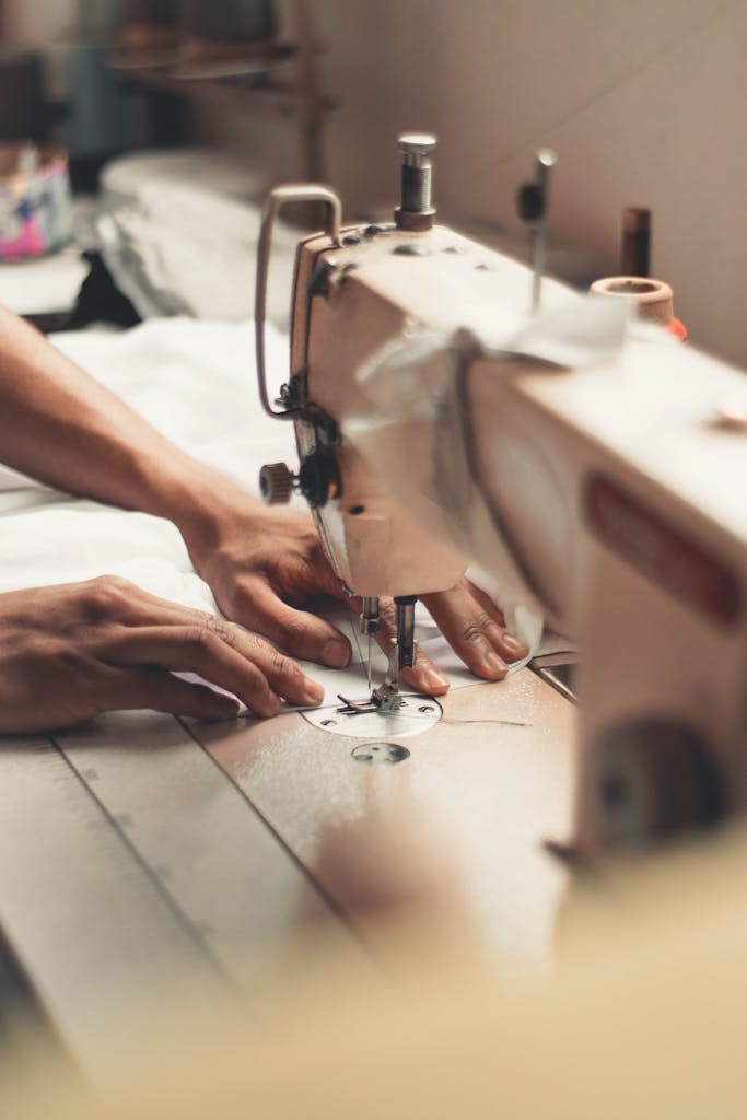 Close-up of hands using a sewing machine, depicting craftsmanship and textiles indoors.