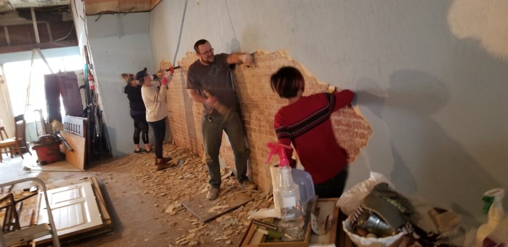 Four people working together to expose a giant antique brick wall