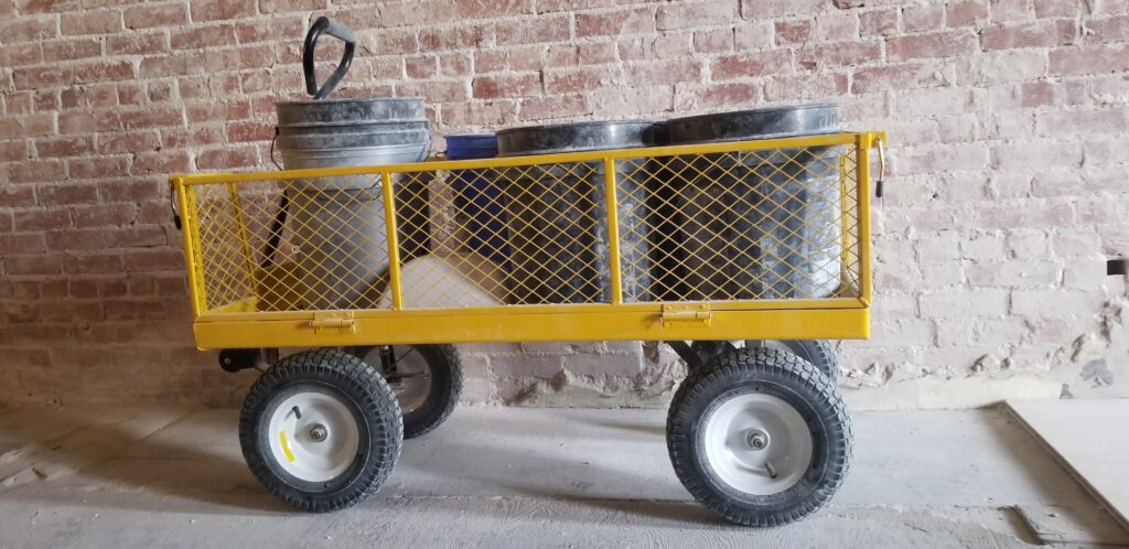 Yellow wagon carrying 5 gallon buckets filled with plaster.