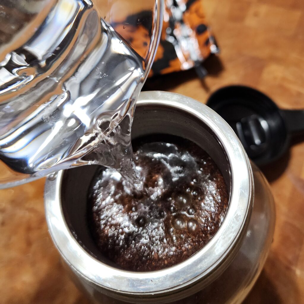 Water is being poured into a strainer with coffee grounds