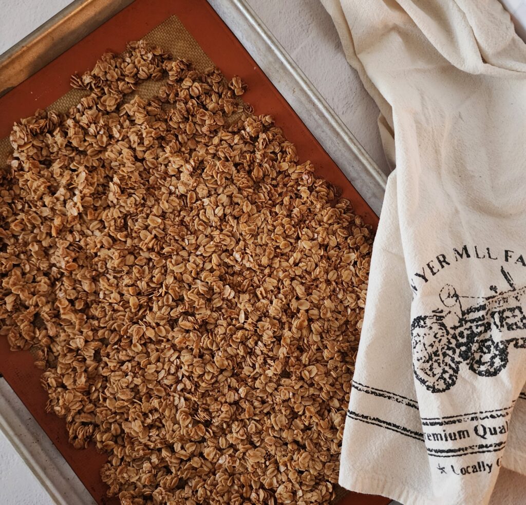 Freshly baked granola on a sheet pan with tea towel