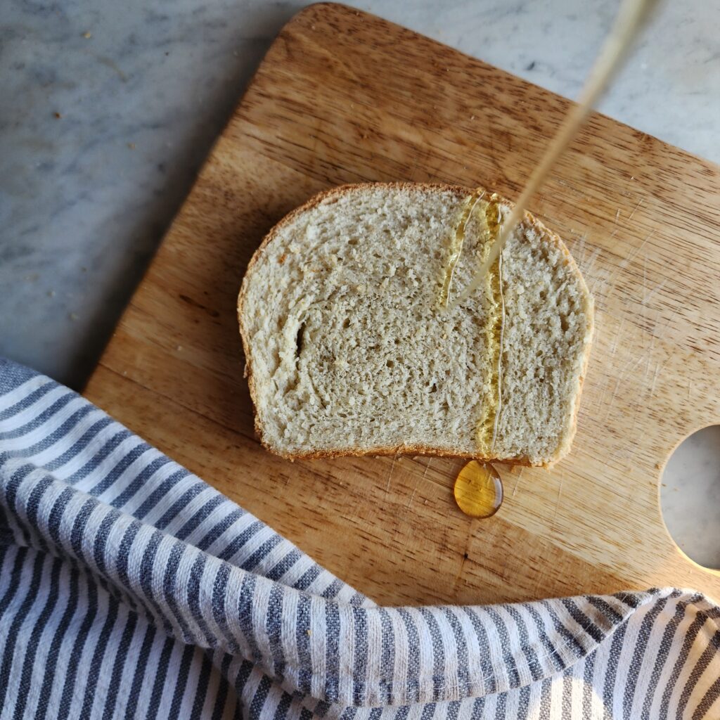 Honey is being drizzled on a slice of Simple Sourdough Discard Sandwich Bread