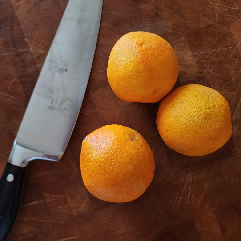 Three oranges sit on a butcher block