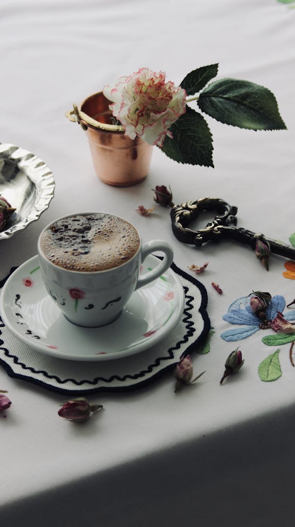 A beautifully arranged still life featuring a coffee cup, key, and floral designs on a table.