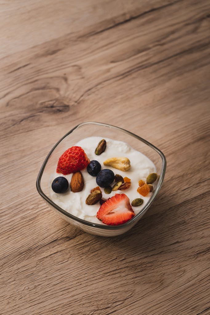 A bowl of yogurt topped with fresh strawberries, blueberries, and assorted nuts on a wooden table.