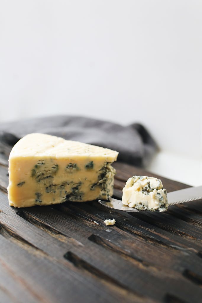 A detailed view of a wedge of blue cheese on a wooden surface with a knife.