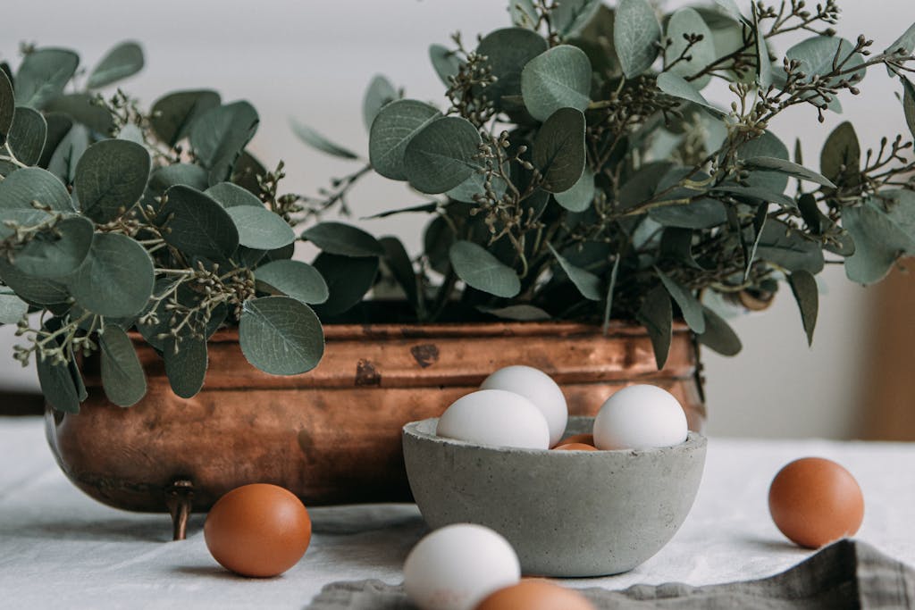 A refined still life with eucalyptus leaves and assorted eggs in rustic bowls, perfect for seasonal decor.