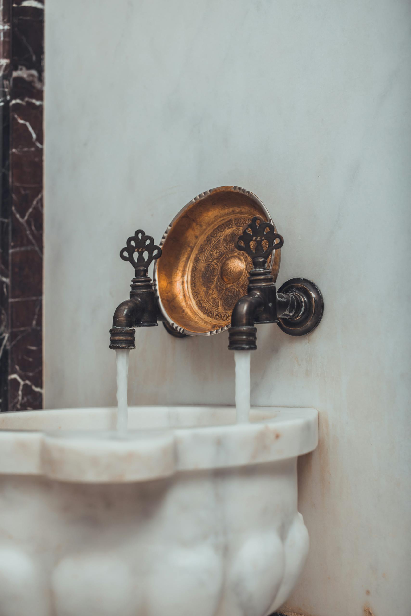 Close-up of a luxurious Turkish bath faucet with water flowing into a marble basin, showcasing traditional design.