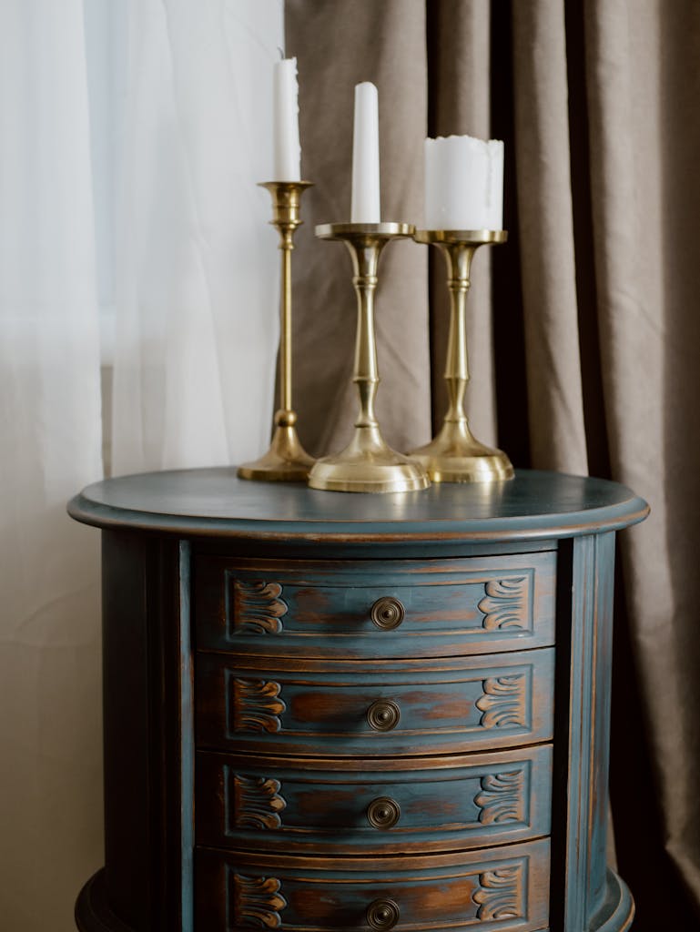 Stylish brass candlestick holders on a blue vintage drawer chest, indoors setting.