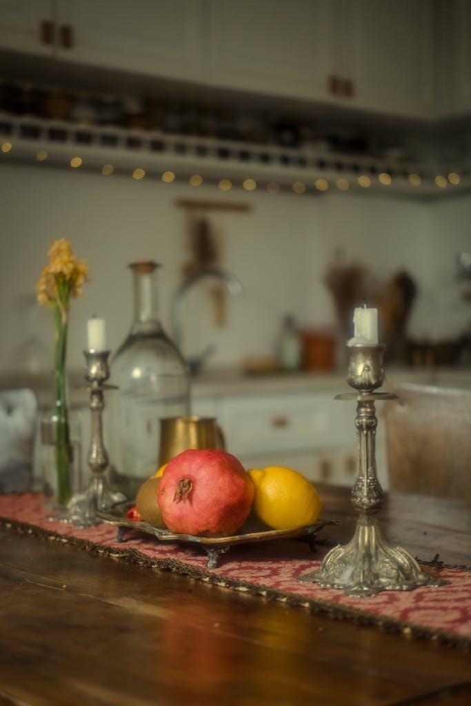 Warm still life of a kitchen table with pomegranate, lemon, and decorative candlesticks.