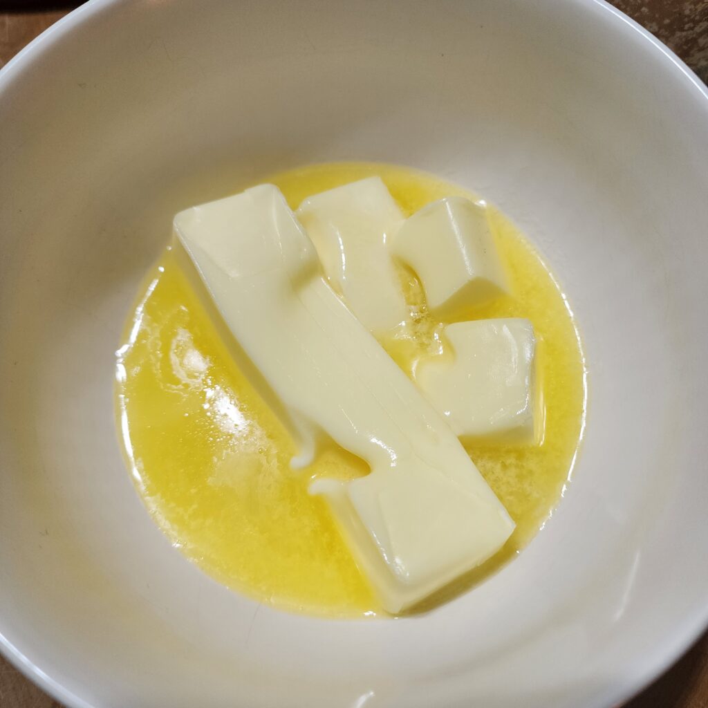 Slightly melted butter sits in a white mixing bowl. 