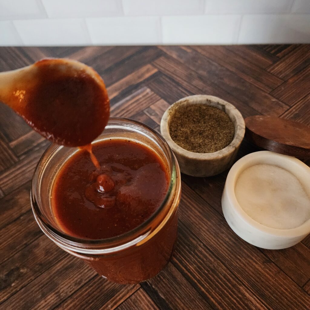 Homemade BBQ Sauce is dripping from a spoon into a Mason jar. 