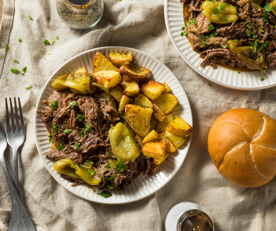 Mississppi pot roast on a plate with roasted potatoes and a roll