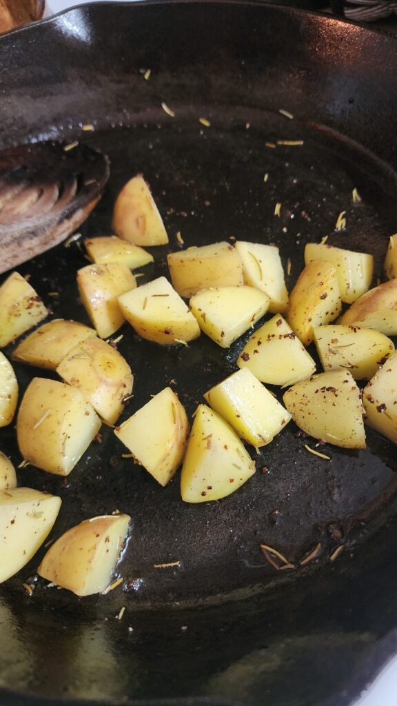 Yukon Gold potatoes chunks are sauteed with olive oil and rosemary in a cast iron plan. 