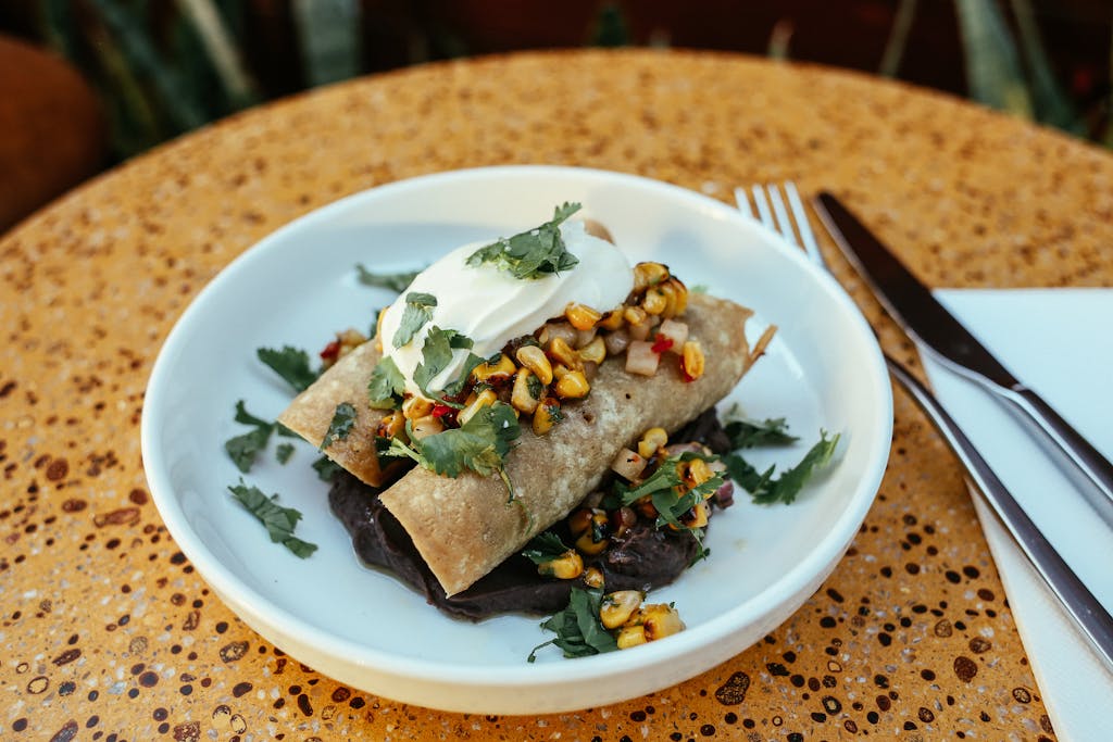 Close-up of enchiladas topped with corn salsa and sour cream, beautifully plated.