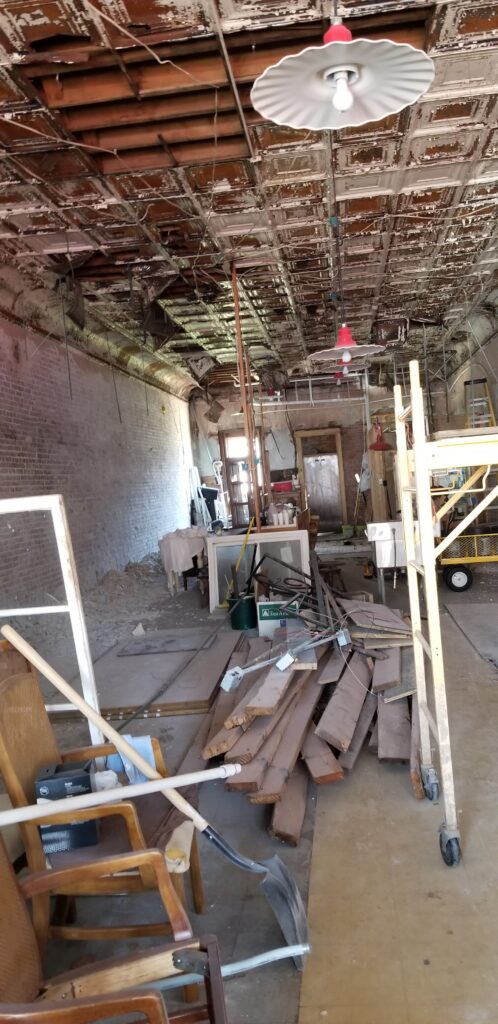 A room with brick walls, construction  materials, and a badly damaged antique  pressed  tin ceiling