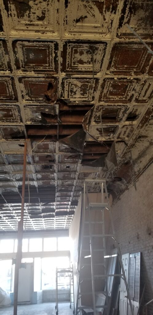 A picture of a badly damaged antique pressed ceiling with rusty tiles, pieces bent and missing 