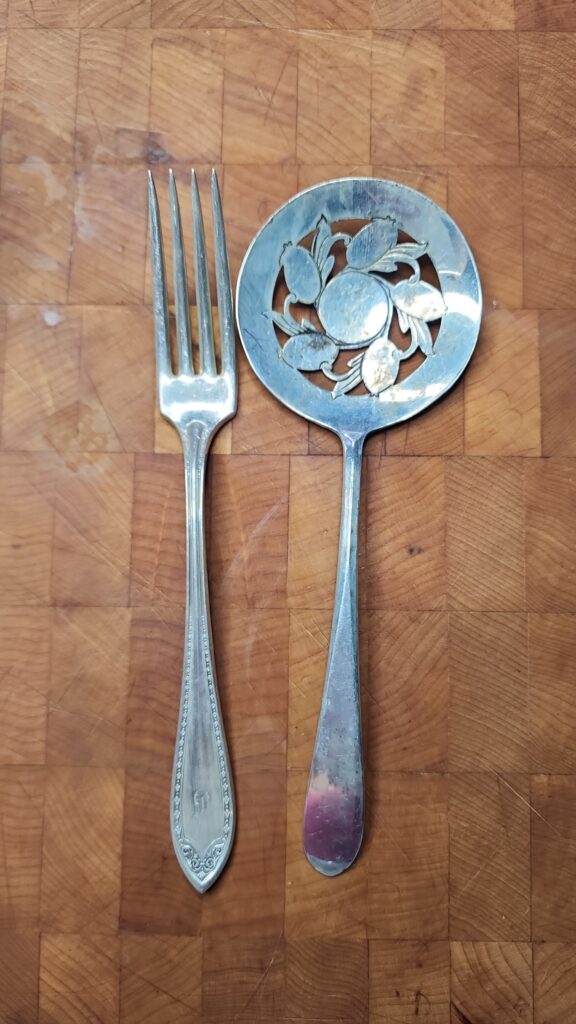 A fork and antique slotted spoon sitting on a butcher block 