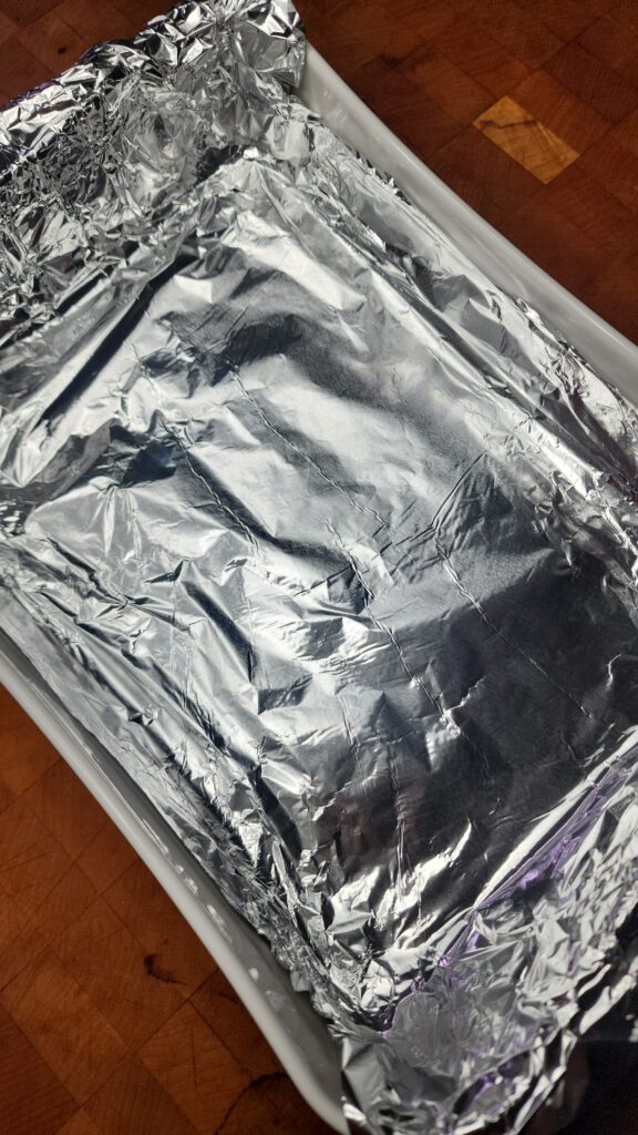 White casserole dish lined with aluminum foil sitting on a ood butcher block 