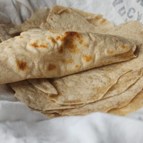 Homemade sourdough tortillas in a bowl with a tea tkwel