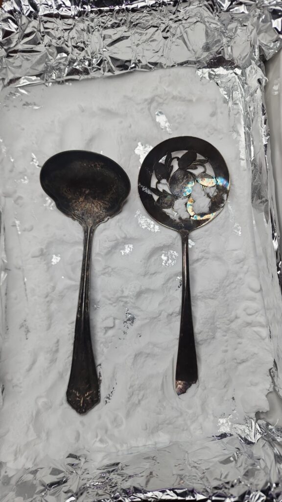 Antique silverware sitting in a casserole dish lined with aluminum foil and baking soda 