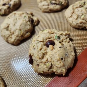 Freshly baked cookies filled with delicious chocolate chips and chopped pistachios are sitting on a silicon baking mat ready to be enjoyed!