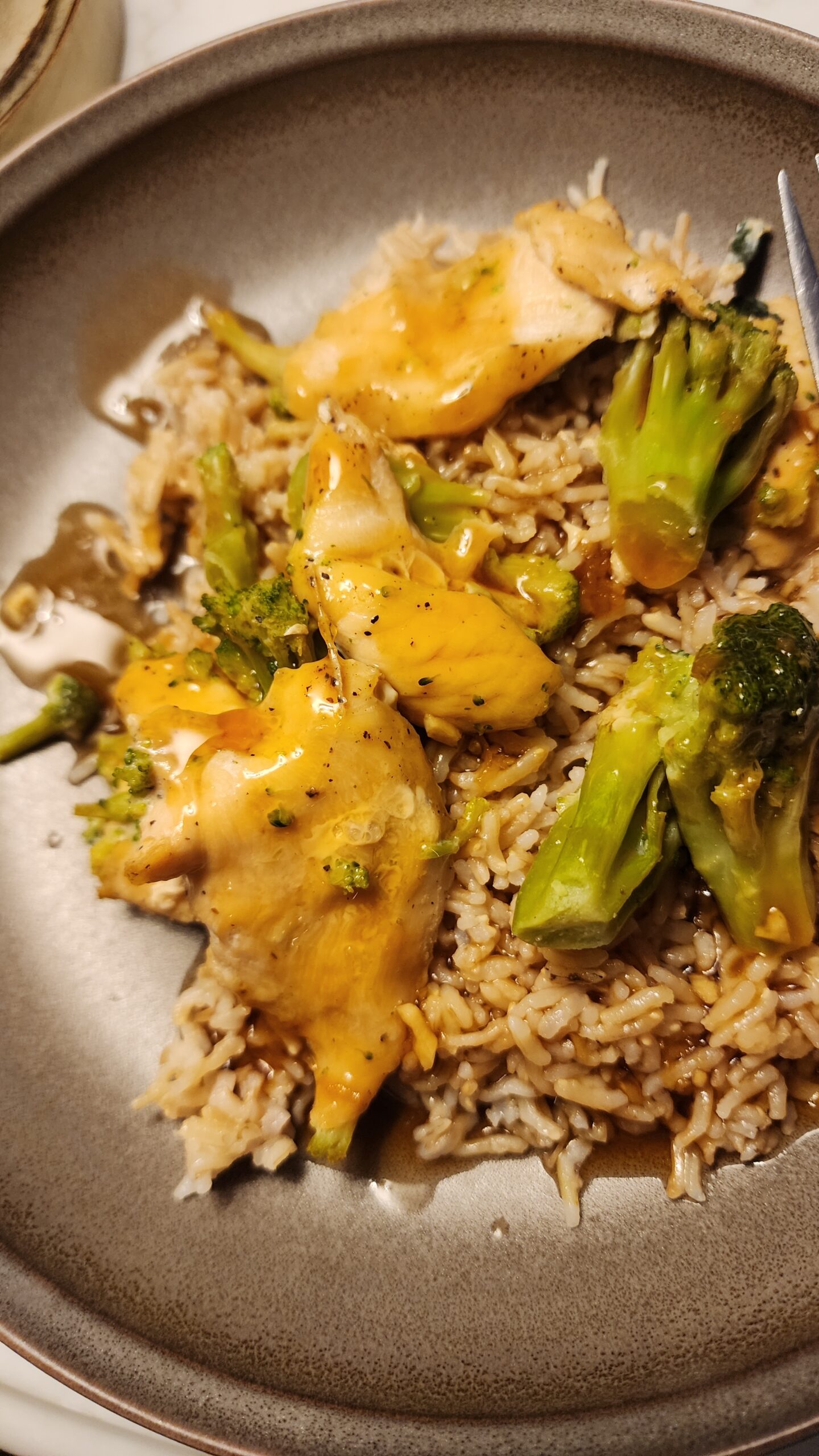 Homemade Teriyaki sauce glazed chicken and broccoli on a bed of rice sits in a brown bowl.