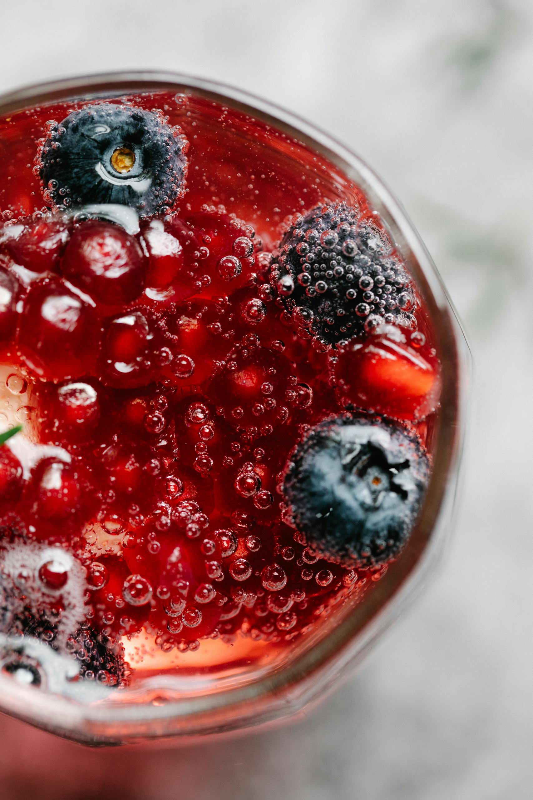 Top view of a bubbly red berry drink with blueberries and currants.