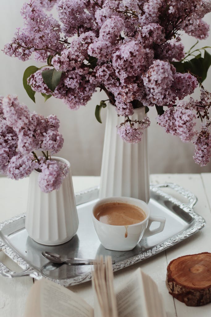 A cozy scene featuring purple lilacs in vases and a cup of coffee on a silver tray.