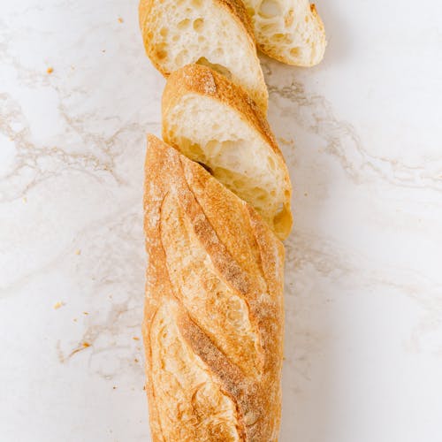 Crispy sliced baguette on a white marble surface in a vertical shot.
