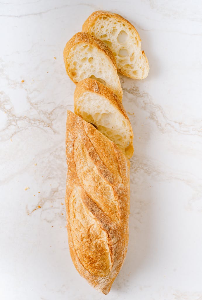 Crispy sliced baguette on a white marble surface in a vertical shot.