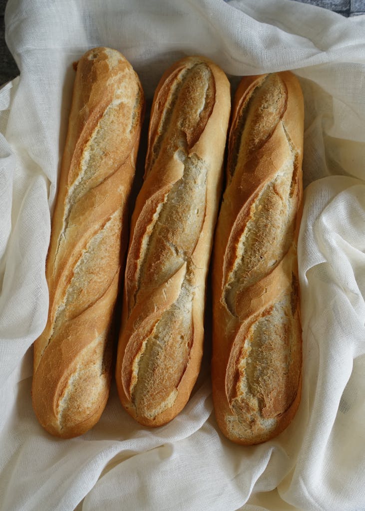 Three freshly baked crusty baguettes resting on a soft white cloth for a rustic look.