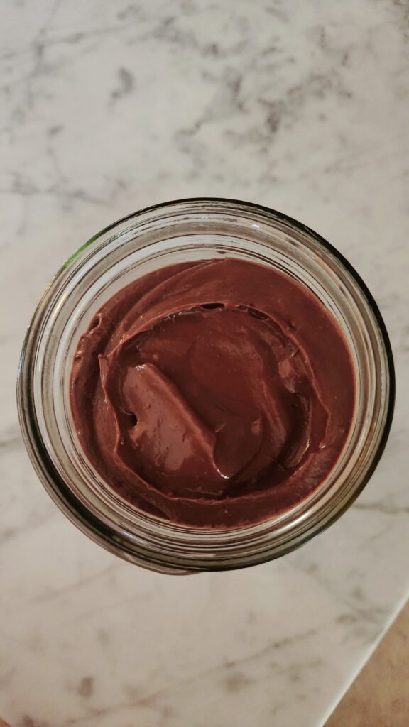 Creamy avocado pudding is in a jar on a marble surface.