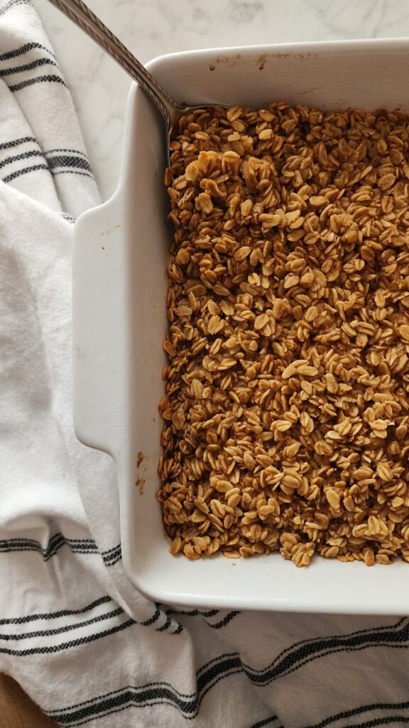A pan of freshly baked Cozy Camp Baked Oatmeal in a white baking pan with tea towel.