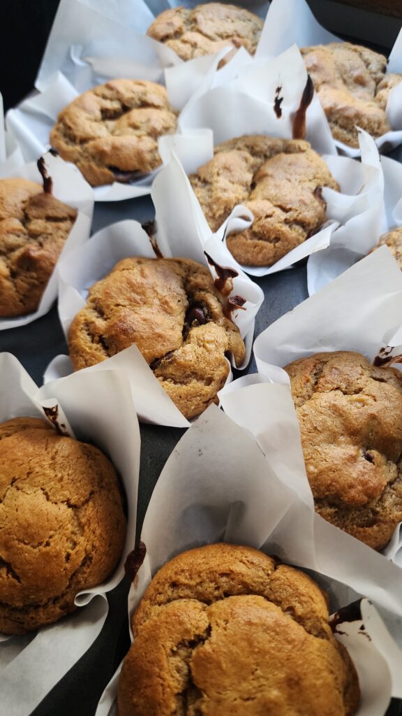 Freshly baked peanut butter banana muffins in parchment paper liners are cooling in a muffin tin.