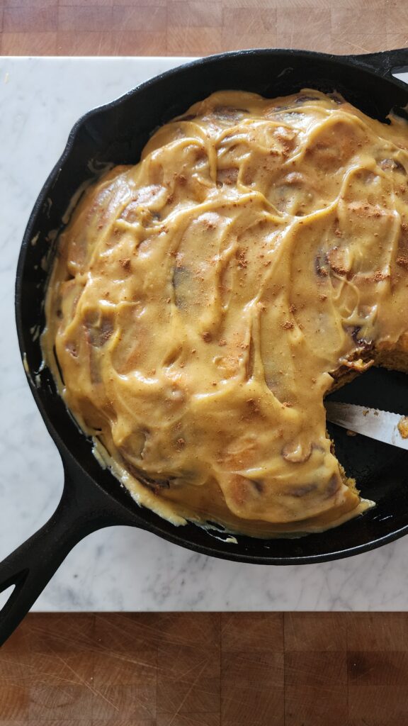 Freshly baked sourdough cinnamon rolls in a cast iron pan on a marble surface