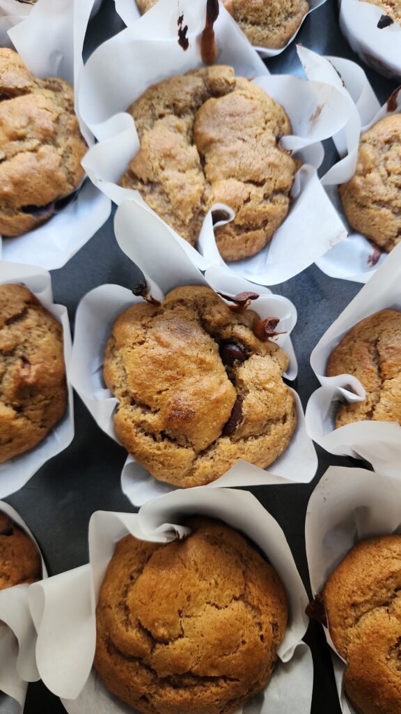 A muffin tin is filled with freshly baked peanut butter banana muffins with parchment paper liners ready to enjoy with a glass of cold milk for the perfect cozy treat.