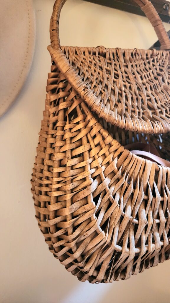 A woven basket hangs on a hook in an entryway and holds a pink dog leash.