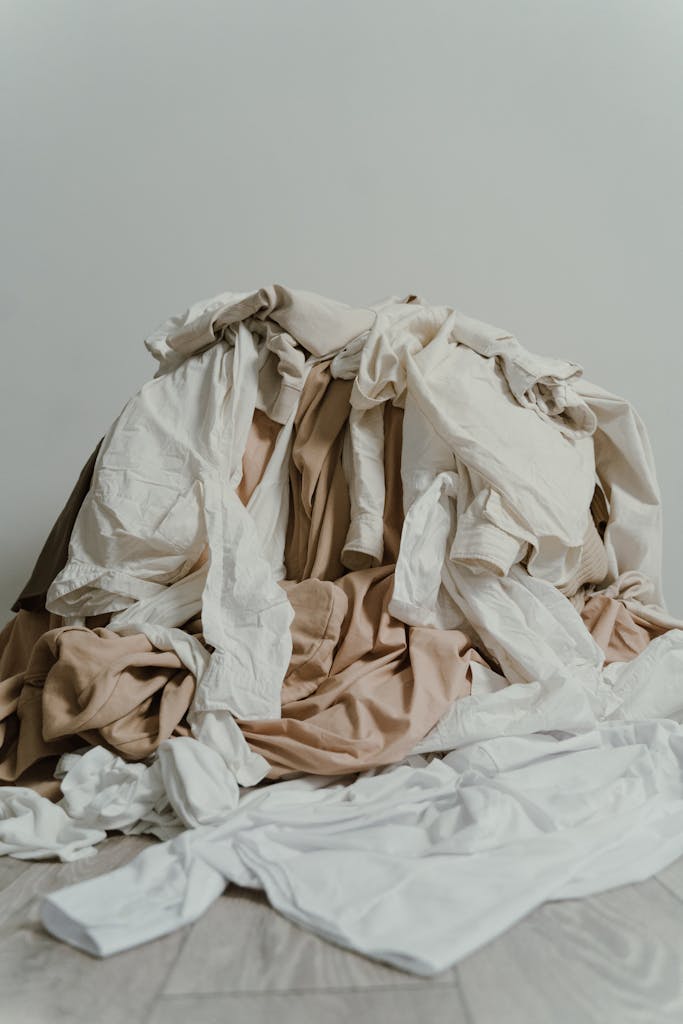 A heap of beige and white clothes casually piled on a wooden floor.