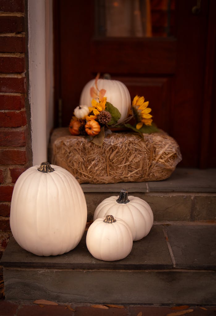Charming fall porch setup featuring white pumpkins and autumn floral arrangement on hay bale.