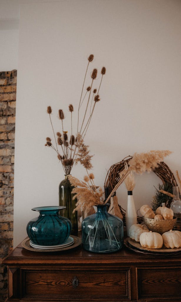 Charming fall-themed arrangement with dried plants, glass vases, and pumpkins on a wooden table.