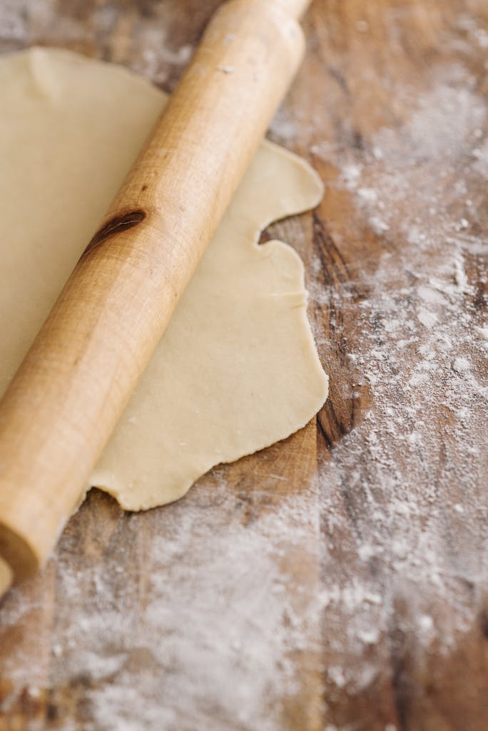 Close-up of rolling pin on dough with flour on wooden surface, perfect for baking themes.
