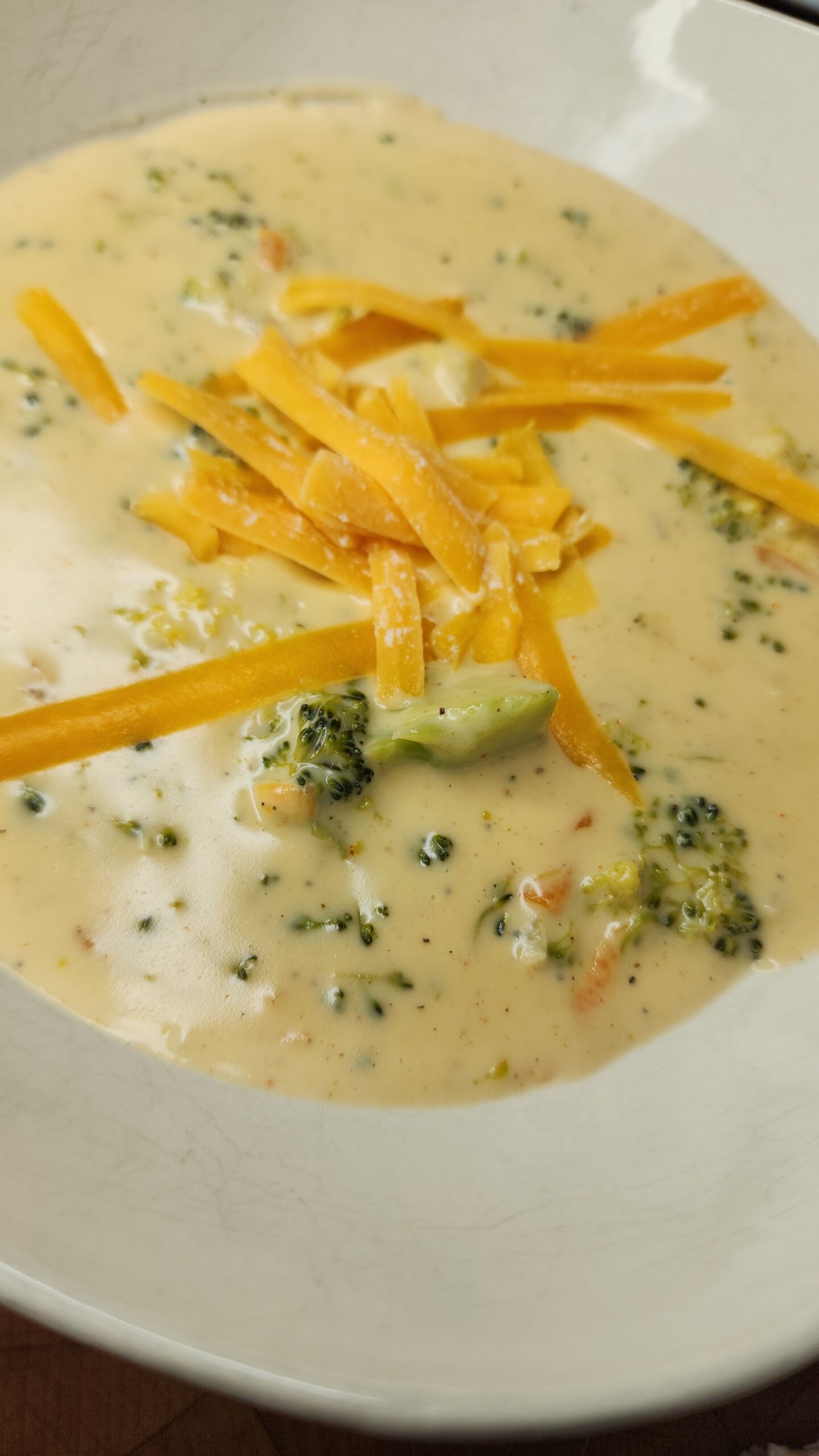 White bowl filled with creamy homemade broccoli cheddar soup, garnished with fresh broccoli florets and melted cheddar cheese
