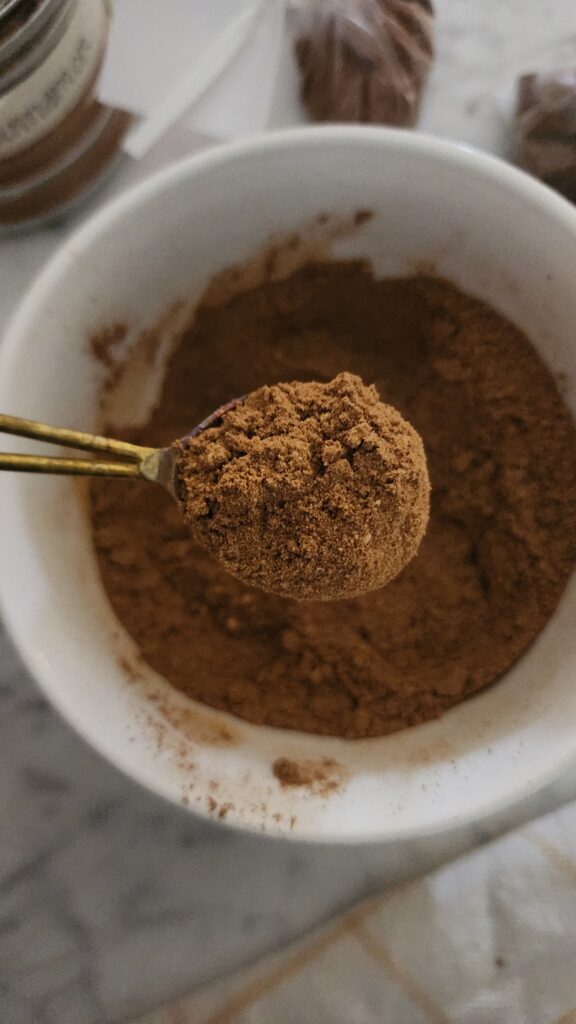 A bowl of freshly mixed homemade pumpkin pie spice being scooped and ready to make a cozy fall recipe.