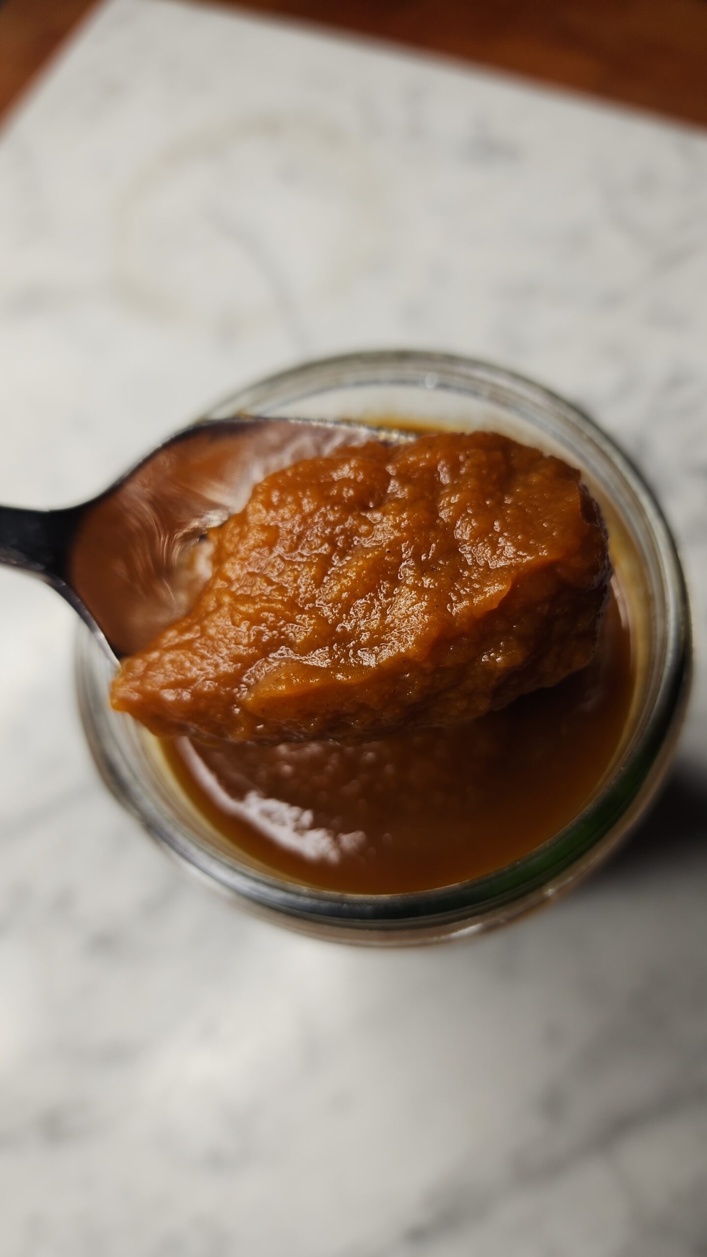 Fresh homemade pumpkin butter is being scooped out of a jar with a spoon on a marble surface.