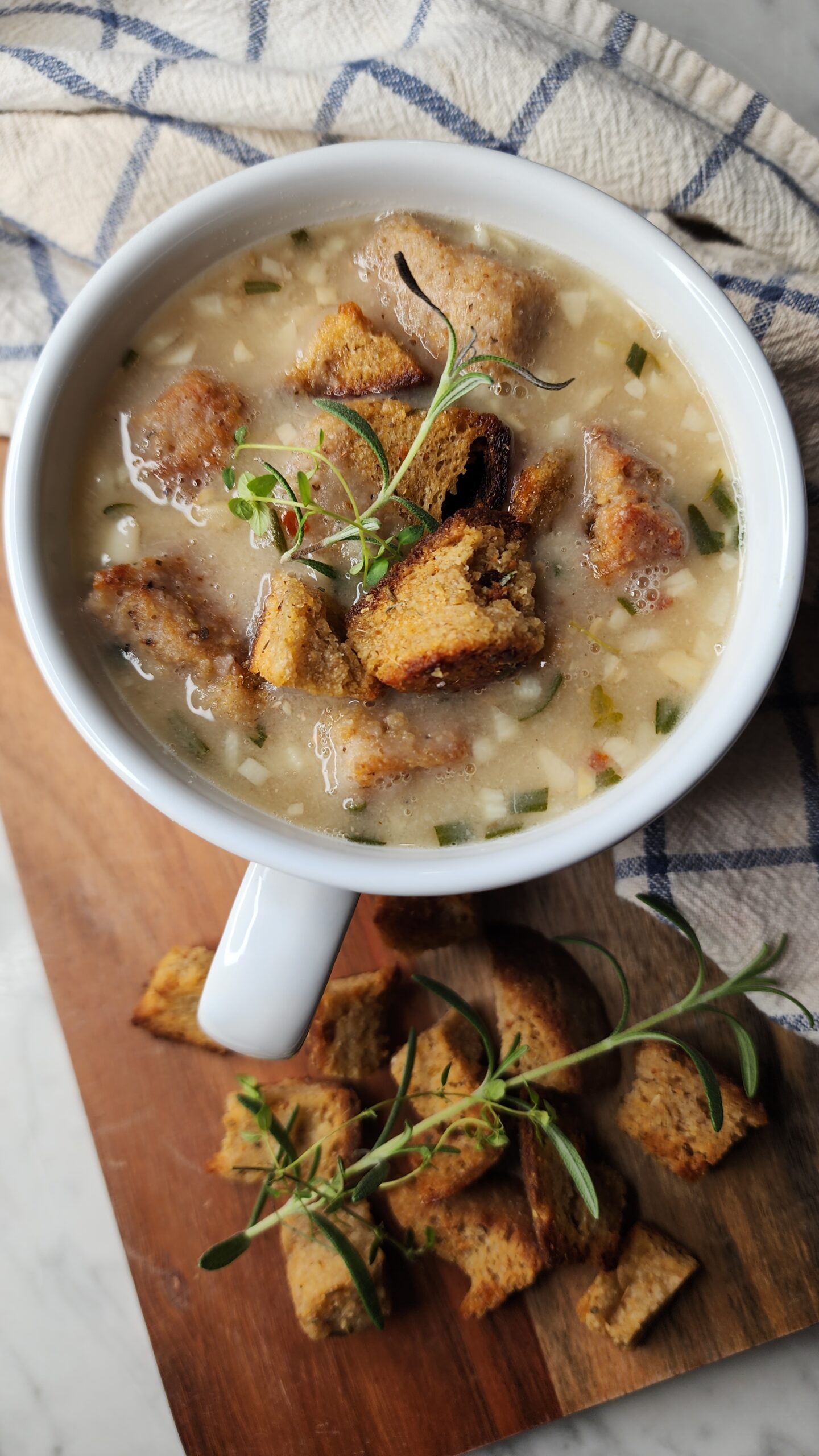 A hearty and cozy bowl of healthy rosemary garlic and white bean soup in a bowl with crunchy homemade croutons topped with fresh herbs.