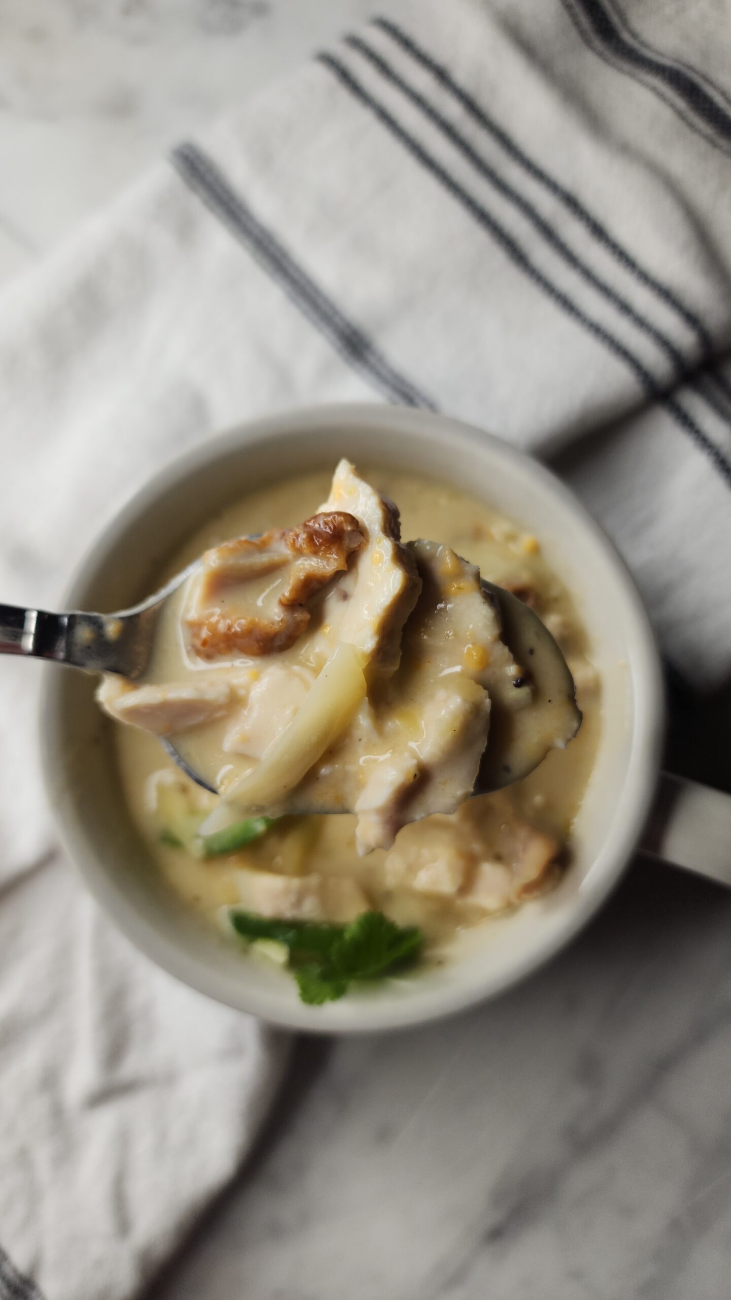 A creamy and delicious bite of keto chicken enchilada soup hovering over a white mug next to a soft tea towel.